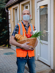 Portrait of a male volunteer in a protective medical mask holding a basket of essential food.