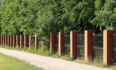 Green garden behind a metal fence with brick pillars
