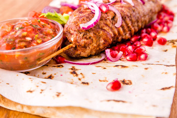 Kebab, meat on a skewer, pita bread, side dish of onions and tomatoes, pomegranate seeds and sauce on a wooden board