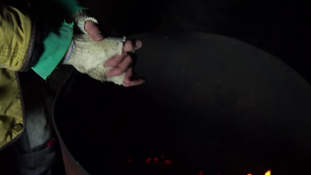 A homeless man warms his hands at night near a barrel of fire. Hands close up.