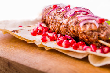 Kebab, meat on a skewer, pita bread, side dish of onions and tomatoes, pomegranate seeds and sauce on a wooden board