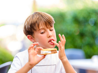 Close up portrait of beautiful boy licking finger while holding and eating sweet ice cream sandwich and looking at ice cream