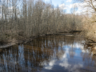 Fototapeta na wymiar river view from the bridge, small river in early spring, blue sky and reflections in the water