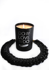 Black decorative candle. Black necklace around the neck. Two objects lie on a white background.