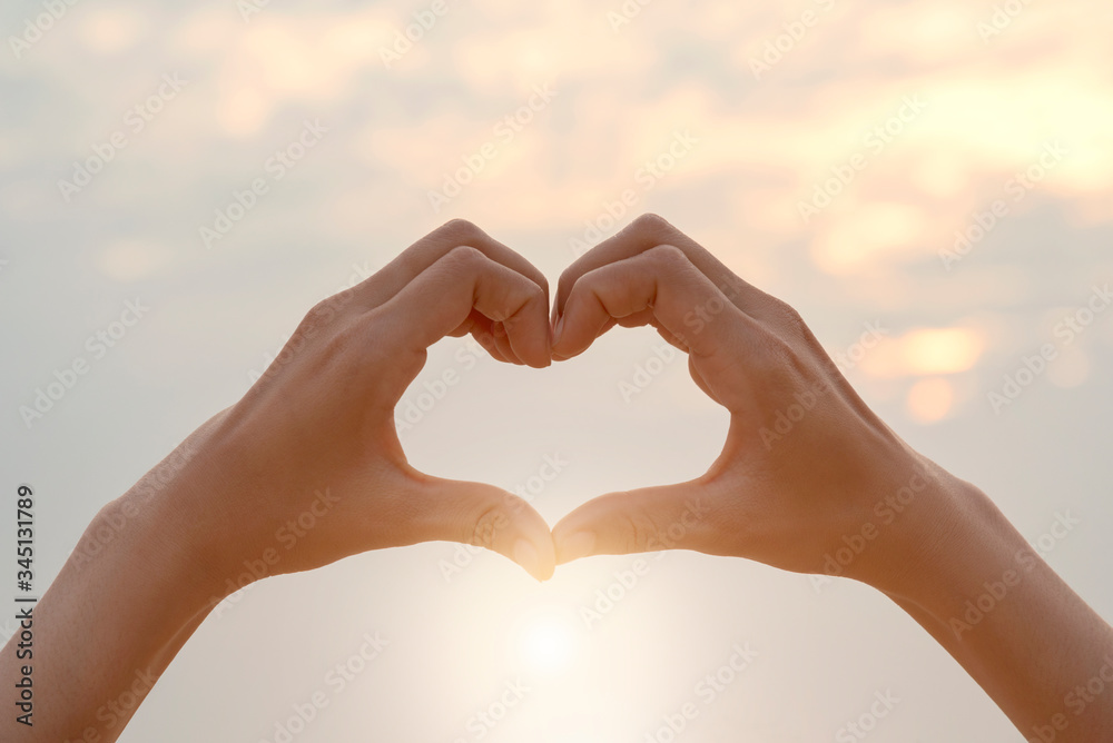 Wall mural Female hands in the form of heart against sunlight in sunset sky, Love concept, Hands in shape of love heart, love Concept, Heart-shape hand gesture