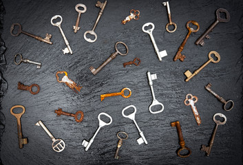 old keys of various shapes and shades seen from above creating a set of shapes on a black stone background
