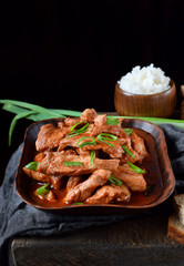 Pieces of meat stewed in tomato sauce with spices served in a clay bowl against black background