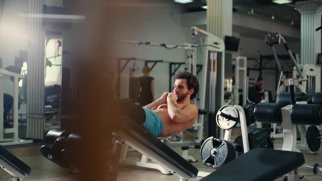 Handsome bearded young man with muscular wiry naked torso doing abs exercises during sport workout training in modern gym. Concept of healthy lifestyle. Tracking shot in slow motion. 