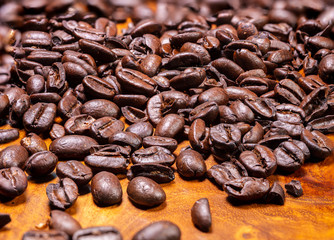 Macro photography of a heap fresh roasted coffee beans on a wooden background. High resolution detailed close up of brown roasted coffee beans on tropical wood table. Background  wallpaper image