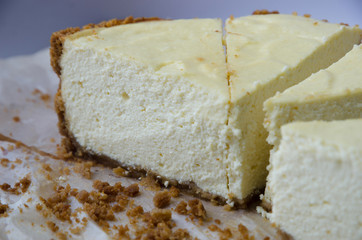 Fragrant homemade cheesecake with chocolate base, cut into pieces, which is lying on a light background.