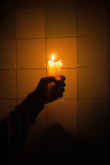 Hand holding the candle against the tiled wall
