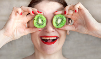 a girl with red lipstick eats a ripe kiwi and jokes with a fruit close up