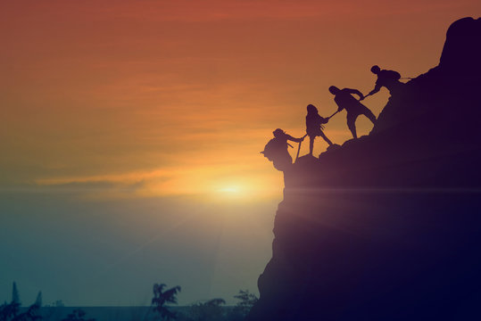 The silhouettes, male and female climbers are using their hands to pull a rope from the steep cliffs of the mountains and have beautiful sunsets, Helps and team work concept. - Powered by Adobe