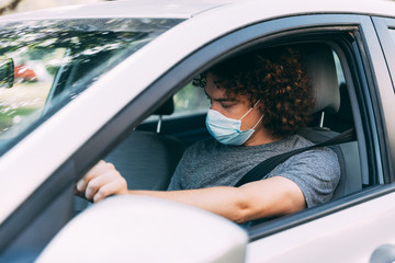 A man drives a car in a medical mask. A man in a protective mask sits behind the wheel of a car. Taxi driver in mask. Protection from coronavirus epidemic pandemic, covid-19. New reality