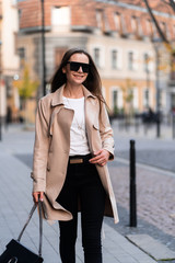 Outdoor photo of brunette lady walking on street background in autumn day.Fashion street style portrait. wearing dark casual trousers, white sweater,creamy coat and sunglasses.Fashion concept.