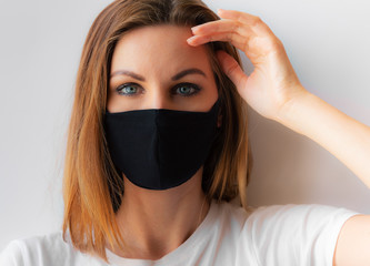 Beautiful portrait of a young woman in a black medical mask and blue eyes and white T-shirt on white background, holds hair by hand. Quarantine, coronavirus epidemic, covid-19. Stay home concept.