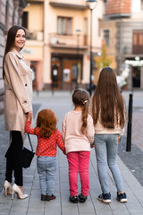 Obraz premium Happy family. mother of many children and three daughters child girl together, walking and joyfully laughing while relaxing on park on a summer holiday. Family outdoors lifestyle. Back view