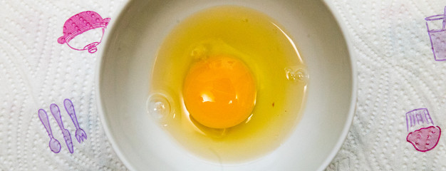 
broken egg in a cup we see yolk and protein, a cup is on the table