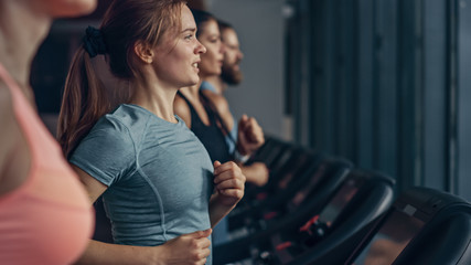 Fototapeta na wymiar Beautiful Athletic Sports Woman Running on a Treadmill. Energetic Fit Female Athlete Training in the Gym. Athletes Workout in Fitness Club. Side View Portrait