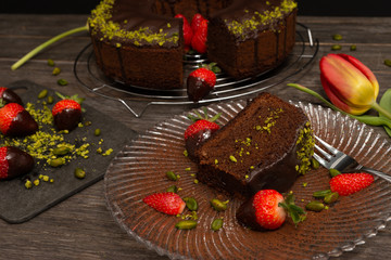 chocolate cake, a slice on a plate, chocolate dipped strawberries and decoration on a table 