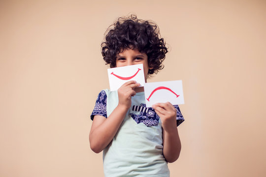 A portrait of kid boy holding cards with positive and negative smile. Children and emotions concept