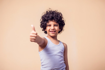 A portrait of smiling kid boy hair showing thumb up gesture. Children and emotions concept