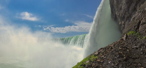 A panoramic view of Niagara falls in Canada from bellow with grey rock, massive waterfalls and blue...