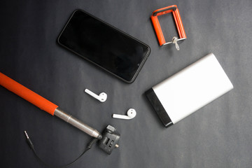 telefono negro, palo selfie rojo, auriculares inalámbricos y bateria externa, accesorios de...