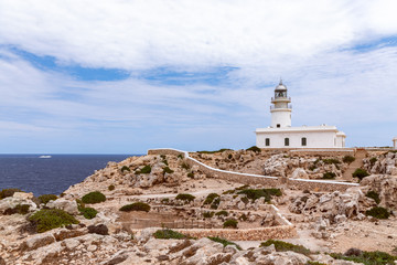 Fototapeta na wymiar Beautiful seascape with a lighthouse (Faro de Cavalleria) on a cliff and a cruise ship in the sea. Menorca, Balearic islands, Spain