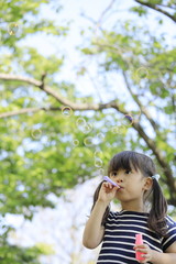 Fototapeta premium 緑の中でシャボン玉で遊ぶ幼児(5歳児)