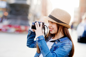 Girl wearing denim coat, straw hat and jeans walking around city center and taking photos 