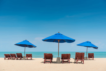 Group of wooden beach bench under parasol umbrella on tropical island beach. Holiday relaxation with turquoise sea and blue sky landscape. Summer vacation travel concept