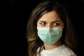 studio portrait of young woman wearing a face mask, isolated on black background.