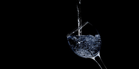 Pour water into glass on black background.