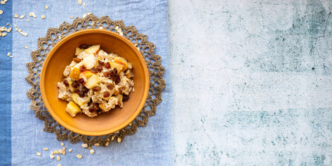 Fototapeta na wymiar Oatmeal granola fruit porridge with banana, apples and raisins. Healthy sweet vegan breakfast. 