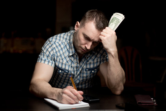 man holds a modest amount of money and makes notes in a notebook