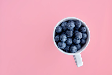Top view a cup filed with blueberries on colorful paper background. Fresh food concept. Copy space.