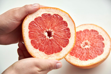 Half of fresh ripe grapefruit in woman's hands on a light background.
