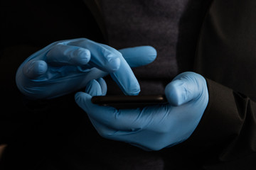 Man wearing PPE protective blue gloves using a touchscreen smartphone during Coronavirus Covid-19 outbreak. Concept for technology during pandemic