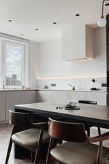 bright kitchen with dark table, convenient location of kitchen accessories and equipment, modern style, White walls, marble working surface and parquet floor. There s a glass of milk on the table and