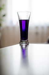 a glass of purple liquid stands in front of the window