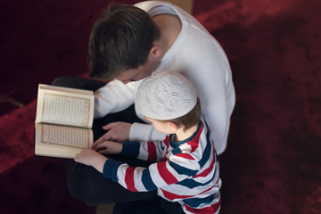 Religious Muslim Man teaching his little son to pray to God with Koran and rosary at mosque during ramadan. © as-artmedia