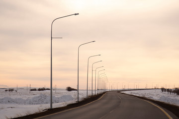 Country asphalt road with lanterns in a field at sunset.