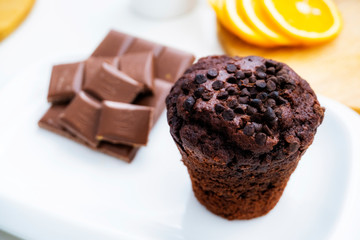 Photo of chocolate muffin in white plate. Cupcake with chocolate closeup. Muffin with chocolate and orange.