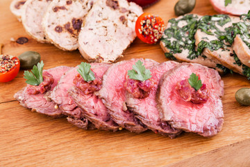 On a wooden plate, beef roast beef, herb marinated tongue, chicken terrine, duck galantin, cherry sauce