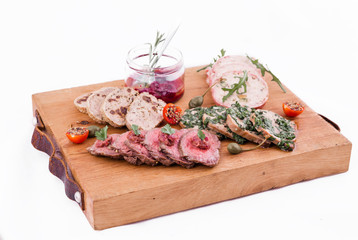 On a wooden plate, beef roast beef, herb marinated tongue, chicken terrine, duck galantin, cherry sauce