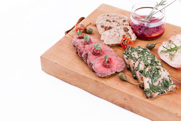 On a wooden plate, beef roast beef, herb marinated tongue, chicken terrine, duck galantin, cherry sauce