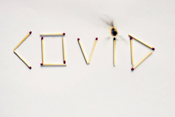 Word covid is laid out of matches on white paper. One match burned out.