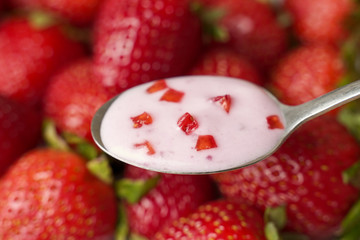 Strawberry yogurt in a spoon, against the background of fresh strawberries