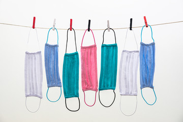 Colorful cotton masks drying on a rope held by Clothes pegs. Reusable fabric masks for coronavirus protection. Handmade multicolored fabric face masks isolated on a white background.